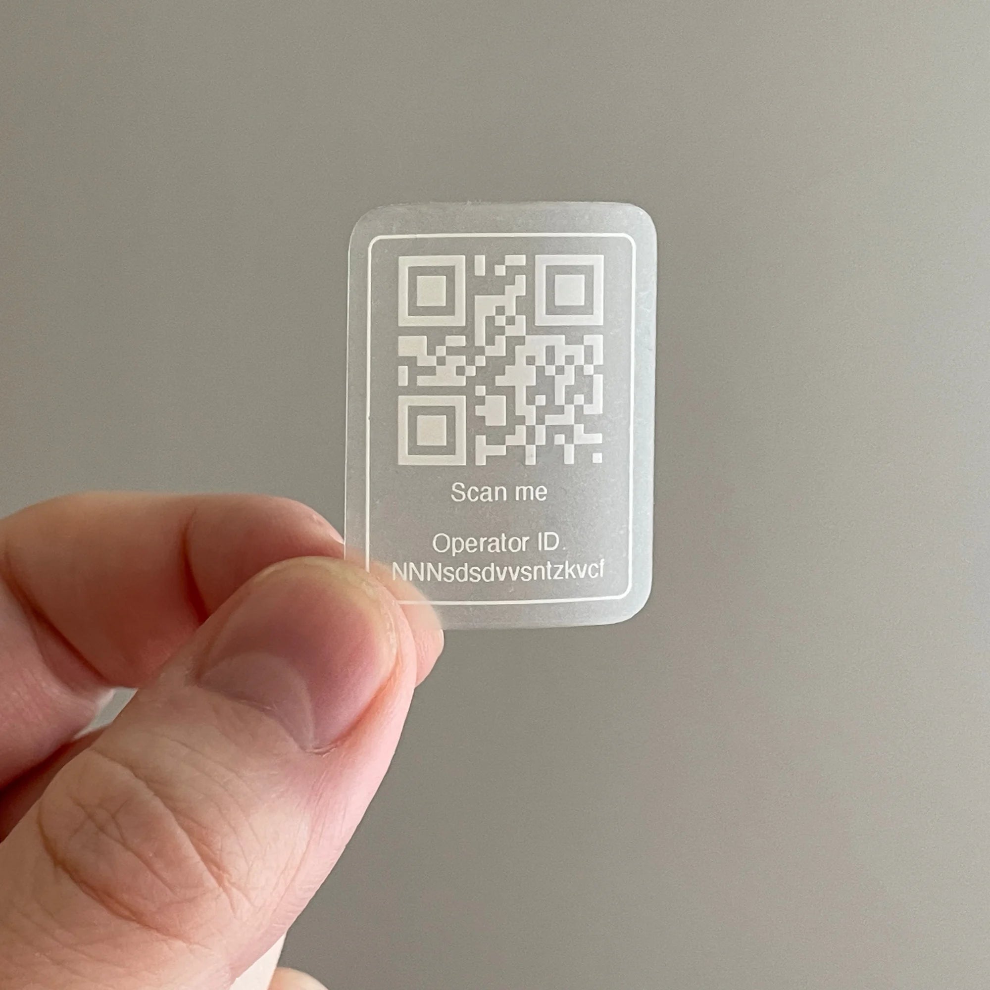 Sticker with a QR code and text held by a hand against a neutral background