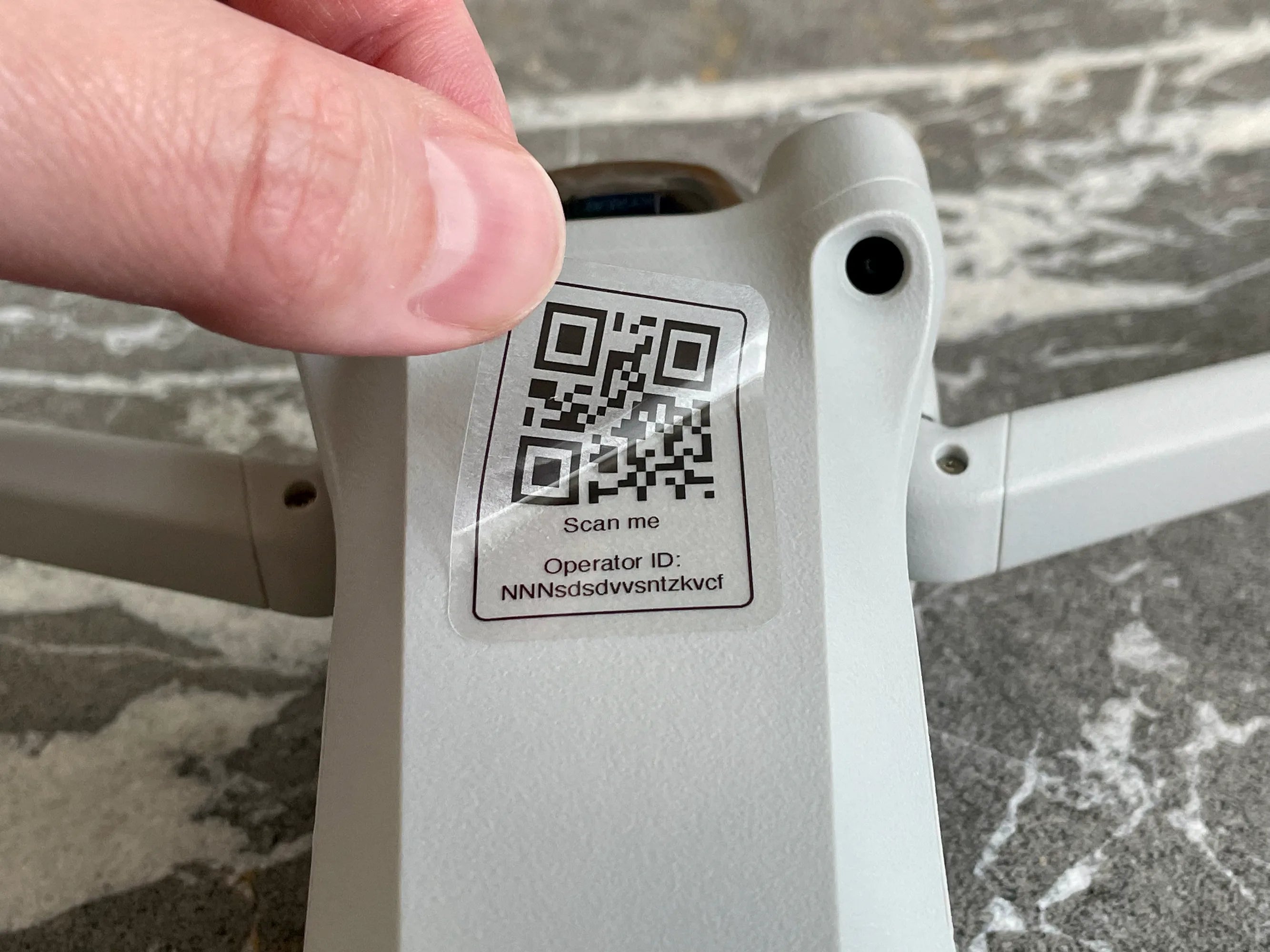 Close-up of a device with a QR code label held by a hand on a marble surface.