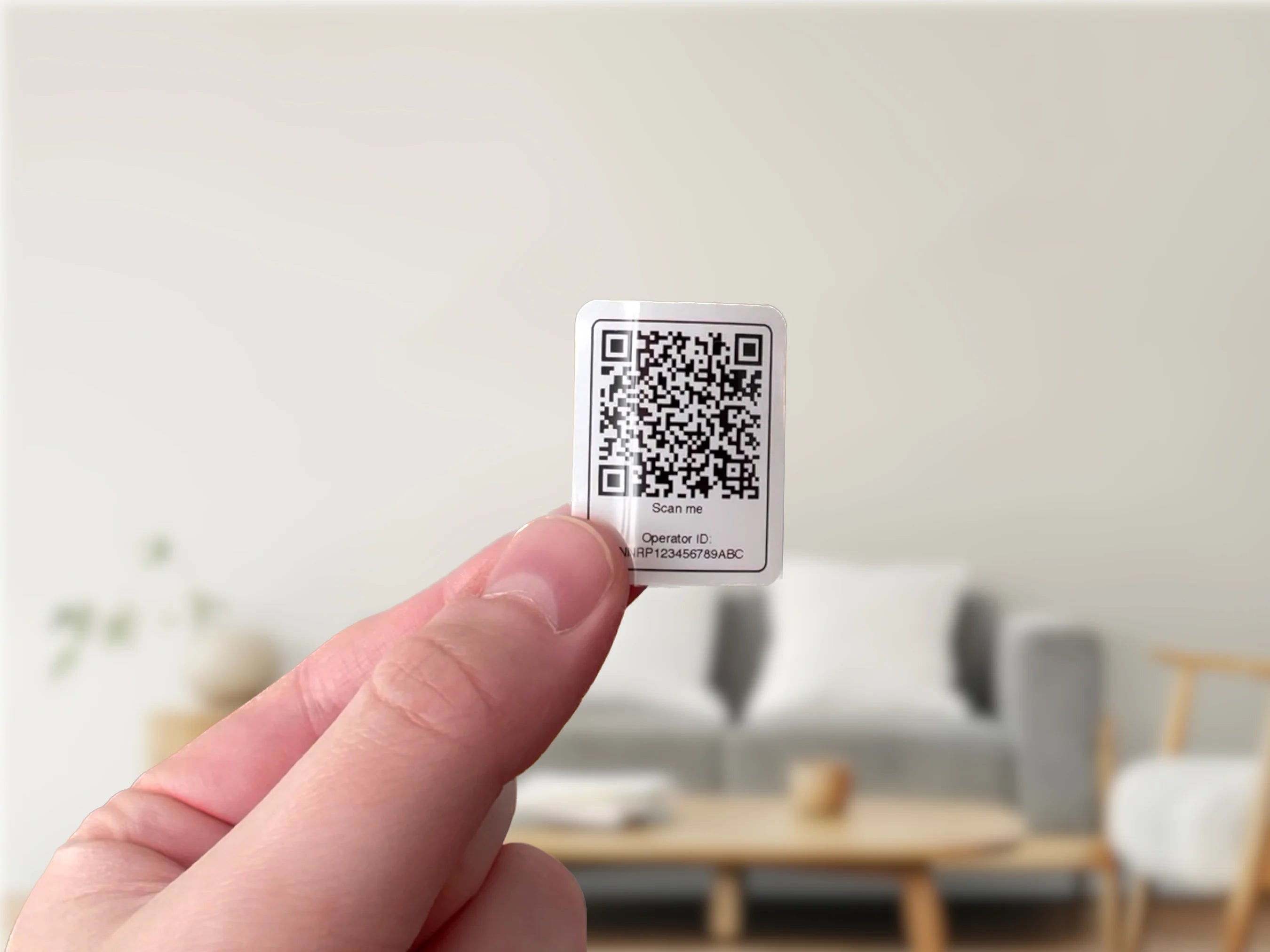 Hand holding a small QR code label against a blurred indoor background